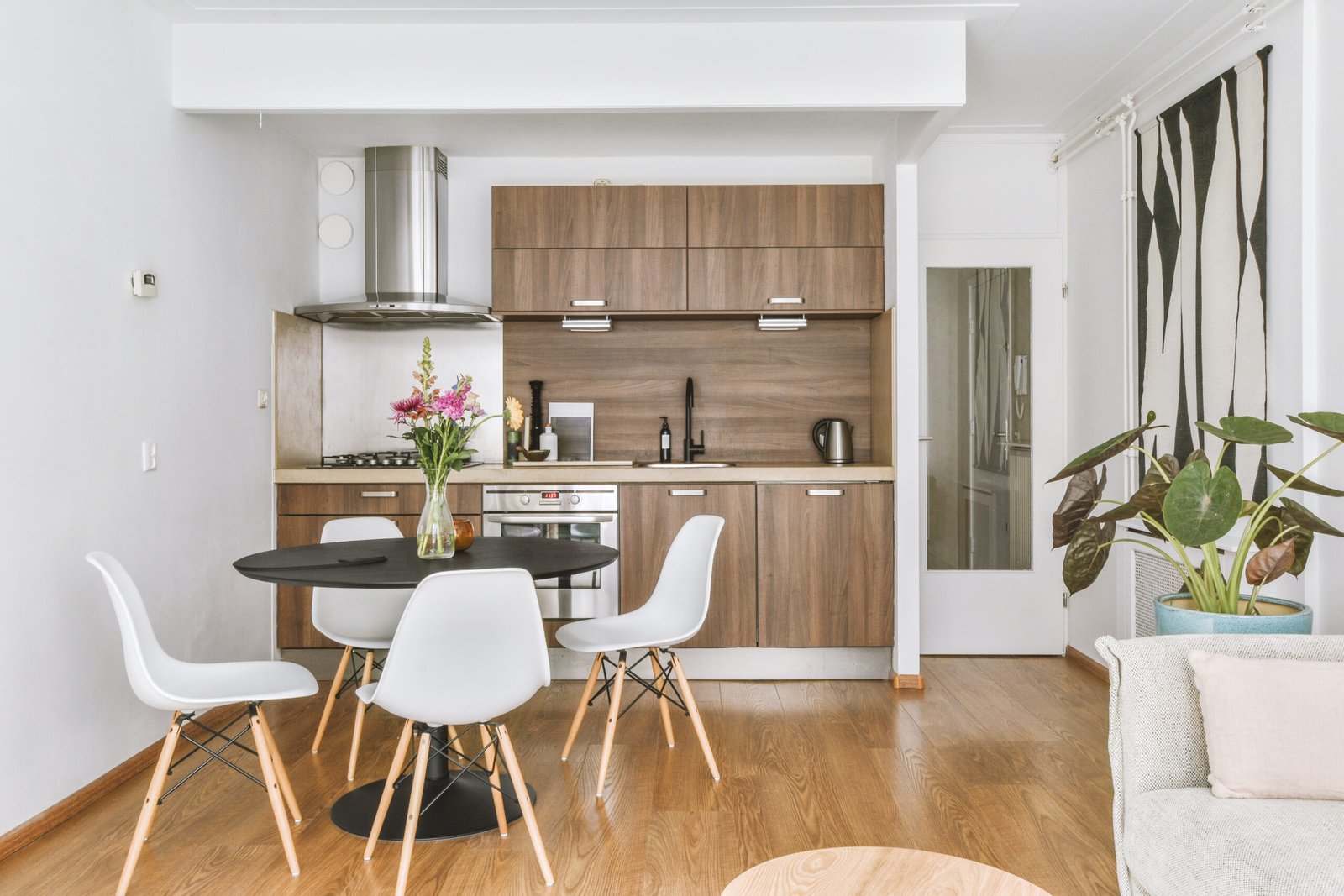 Table with chairs and flowers located near lounge area and kitchen in spacious room of contemporary apartment